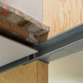 Close-up of a metal building beam connected to a wood stud wall with exposed brick and plaster.